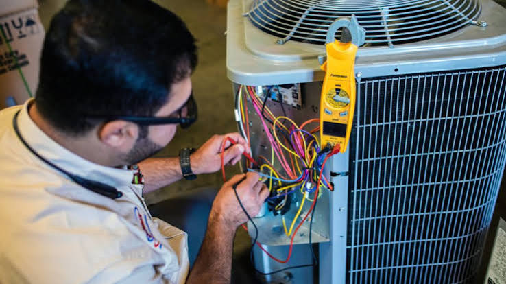 Technician testing the electrical wiring of an outdoor air-conditioning condenser