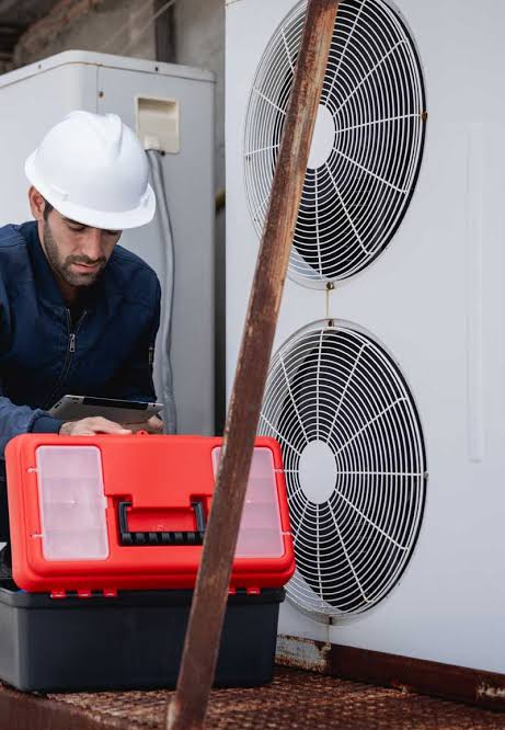 Technician in a hard hat working beside a large outdoor air-conditioning unit