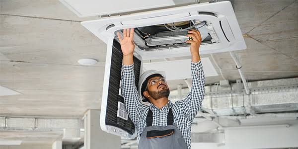 Technician servicing a ceiling-mounted HVAC unit and its airflow components