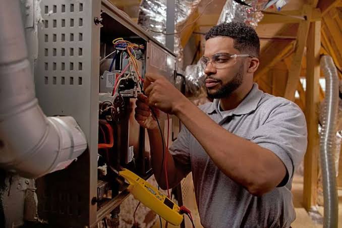 HVAC technician repairing wiring and controls inside a residential furnace