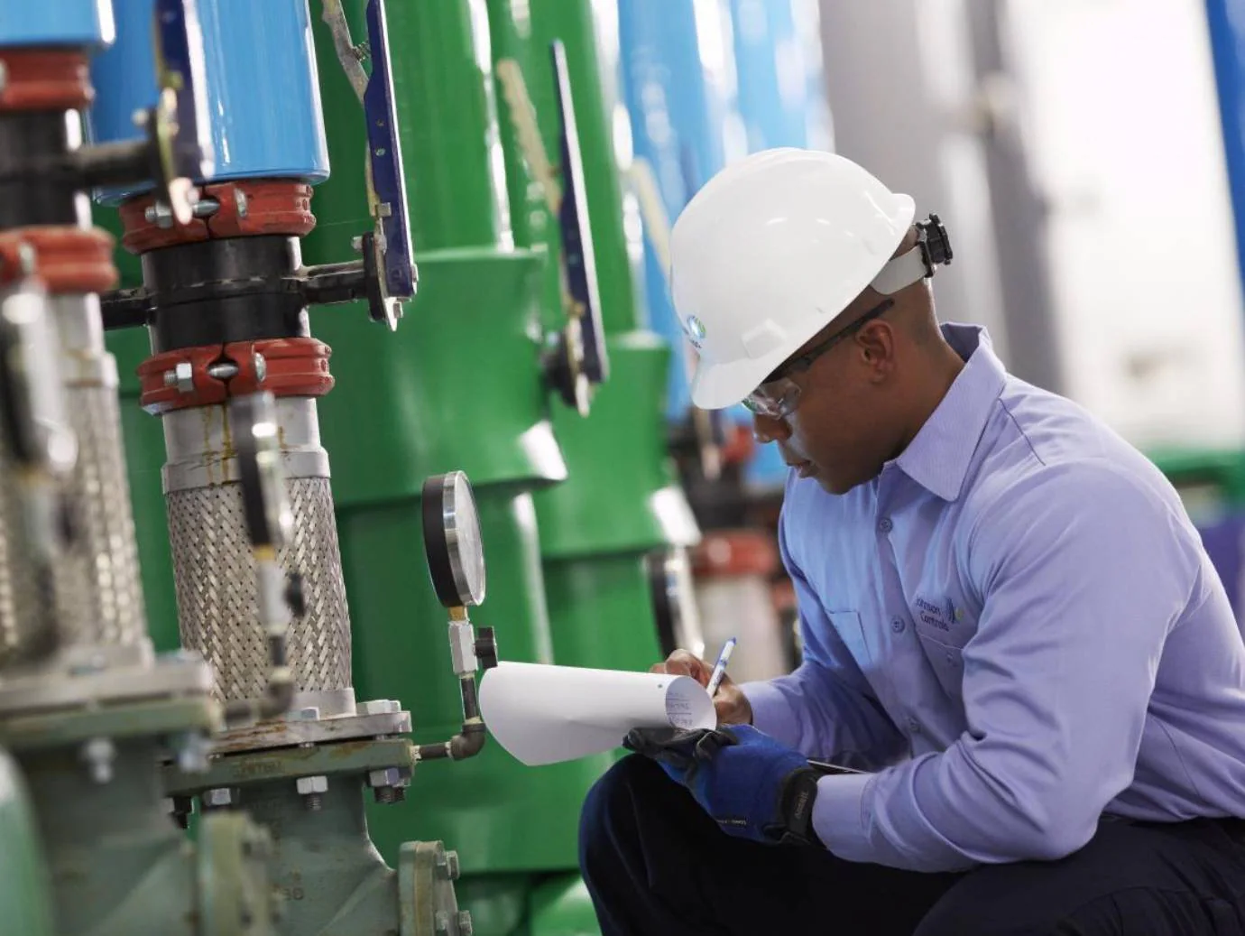 HVAC professional recording equipment readings beside mechanical piping